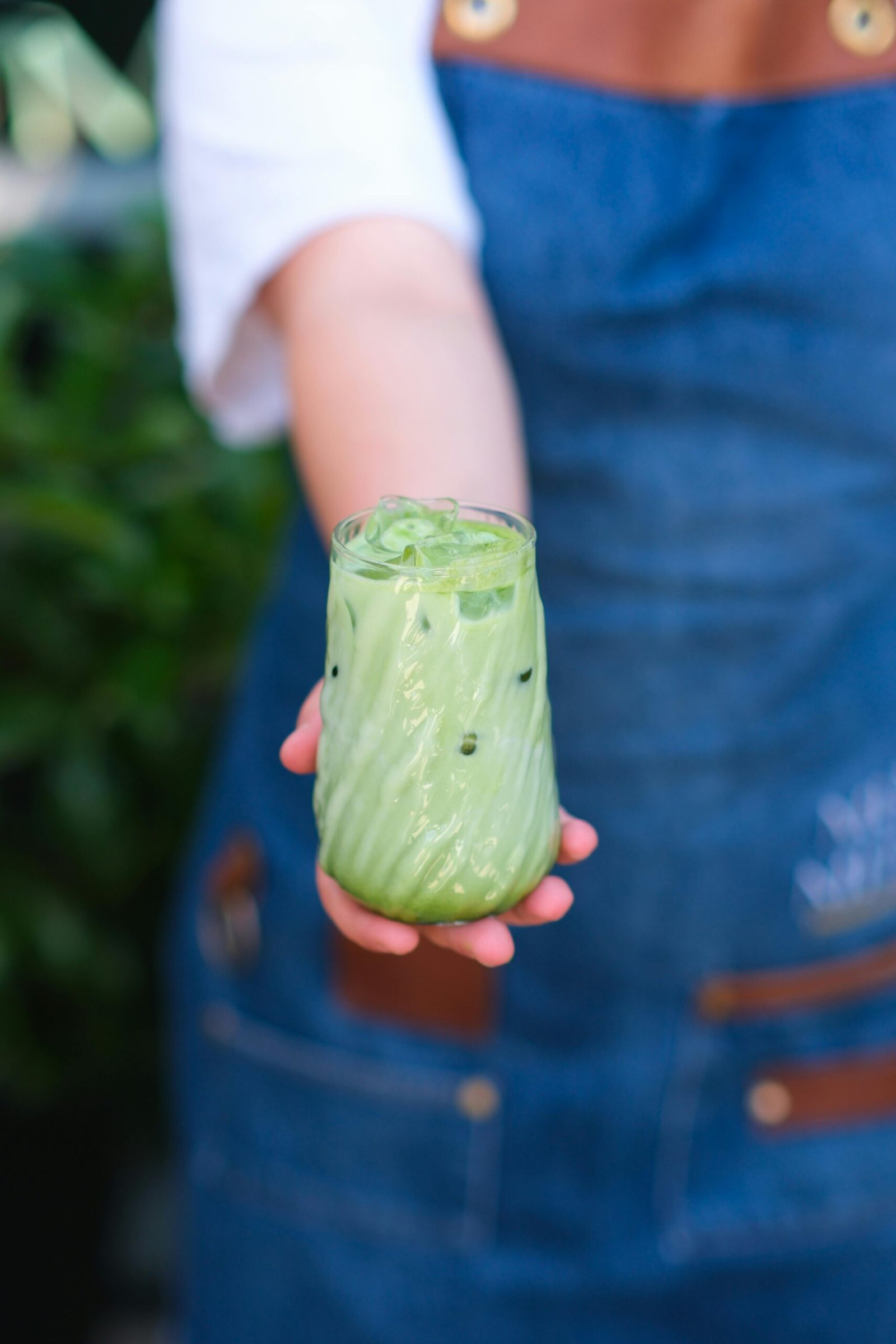 A close-up of a hand holding a refreshing iced matcha latte in a garden setting.
