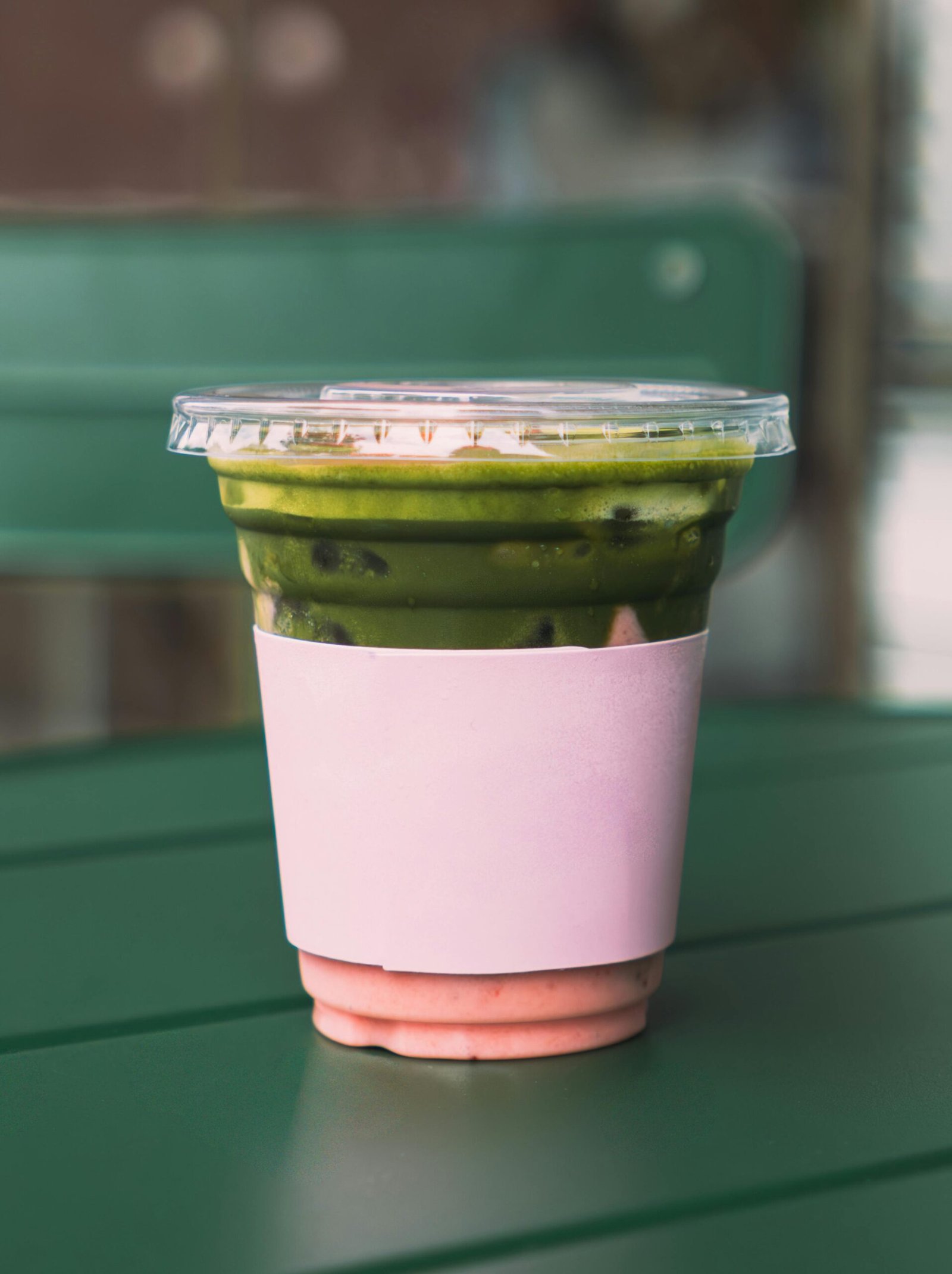 A refreshing iced matcha latte with a pink sleeve on a green table, captured in an outdoor cafe setting.